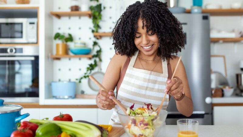 \Close up portrait of happy young woman while she try tasty vegan salad in the kitchen at home.